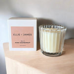 Glass candle with 'Ellie + James' packaging on a wooden surface.