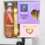 A gift box containing a bottle of sparkling ginger and peach drink, passionfruit shortbread bites, coconut ice, and a white chocolate Sante bar. The box is presented with a purple ribbon and a keepsake card.