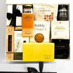 Gift basket with various items including chocolate, nuts, and a soap bar on a white surface.
