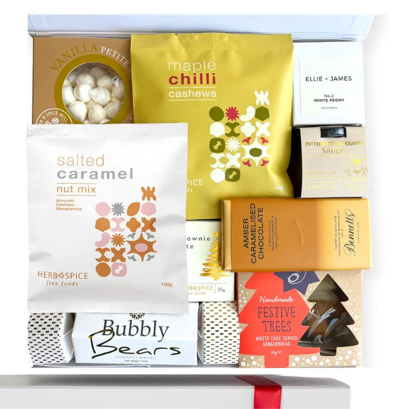 A gift box containing a variety of food items including gingerbread trees, salted caramel nut mix, butterscotch and brandy sauce, chocolate brownie bite, champagne bears in a Christmas cracker, vanilla meringues, maple and chili cashew nuts, and a handmade candle, all packaged in a white box with a gold seal and ribbon.
