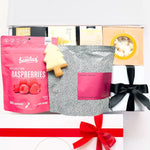 Gift box with assorted items including a pink bag of raspberries and a black and white patterned pouch.
