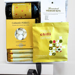 Assorted food items including caramel pebbles, maple chilli cashews, and Whitaker chocolate bars in a box.