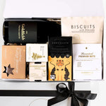 A luxury white gift box with magnetic closure containing a variety of festive treats including a wine bottle, brownies, a chocolate box, biscuits, a chocolate bar, and a keepsake gift box with a gold seal and ribbon.