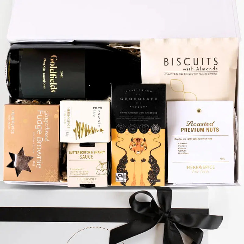 A luxury white gift box with magnetic closure containing a variety of festive treats including a wine bottle, brownies, a chocolate box, biscuits, a chocolate bar, and a keepsake gift box with a gold seal and ribbon.