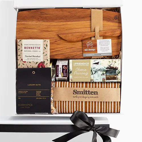 A luxury gourmet picnic gift box from Raine & Horne, featuring a wooden cheese board, a linen tea towel, a honey trio box, a luxury nut mix, fig relish, and organic chocolate.