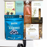 An assortment of gourmet food items in a gift box, including Bennetts dark chocolate bar, Mangawhai sea salt chocolate, Arepa sparkling ginger and peach drink, roasted premium nuts, blueberries, and Herb and Cheese straws.