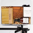 Gift set with a bottle, wooden spoon, and striped towel in a box with a black ribbon.