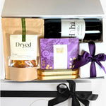 Gift basket with wine, snacks, and a book tied with a purple ribbon.