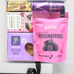 Assorted snacks including a pink package of boysenberries, a purple box of passion fruit shortbread bites, and other branded items on a white background.