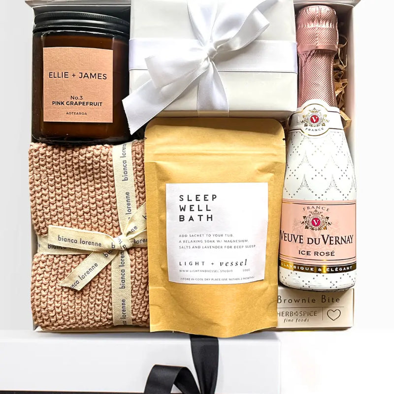 Gift set with a bottle of champagne, candle, bath salt package, and knitted blanket.