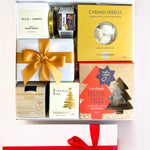 A luxury white gift box with magnetic closure containing a variety of Christmas treats, including a candle, caramel pebbles, butterscotch and brandy sauce, gingerbread Christmas trees, chocolate brownie bite, and fig relish, all decorated with a gold ribbon and a personal message card.