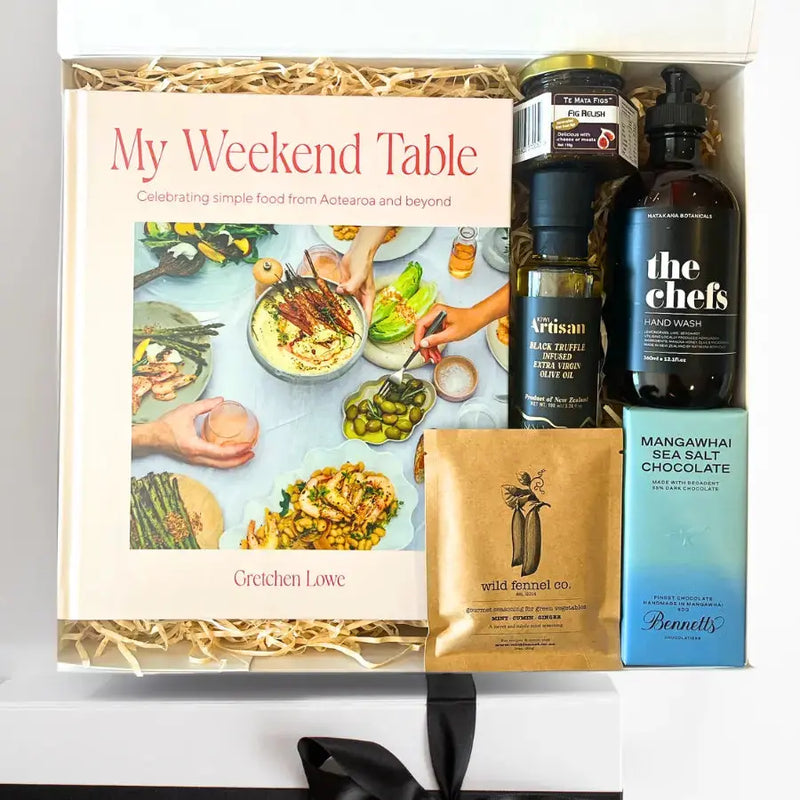 Gift box with 'My Weekend Table' book, bottles, and other items on a white background