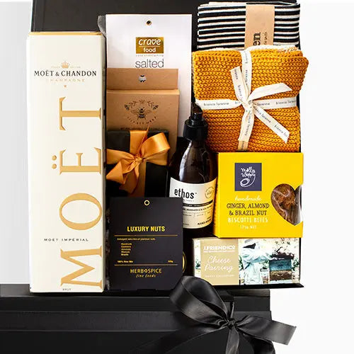Gift basket with Moet & Chandon champagne, snacks, and other items on a black surface.