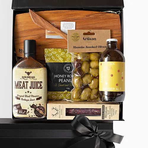 A luxury gift box containing a variety of gourmet food items including barbecue sauce, cheese board, honey roasted peanuts, smoked olives, salami, and ginger ale.