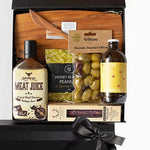 A luxury gift box containing a variety of gourmet food items including barbecue sauce, cheese board, honey roasted peanuts, smoked olives, salami, and ginger ale.