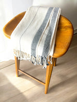 Turkish Towel with blue and white stripes draped over a wooden chair on a light wooden floor.